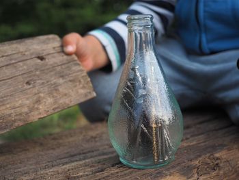 Midsection of boy with nails in glass bottle on wooden table
