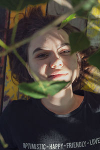 Close-up portrait of young woman lying by below leaves