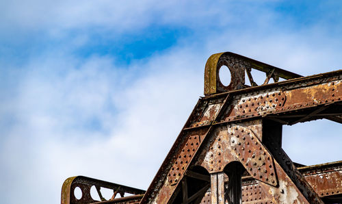 Old rusty iron bridge structure set against blue sky