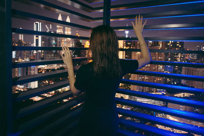 Rear view of woman standing at balcony during night