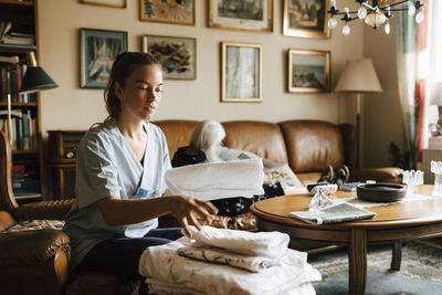 Female caregiver arranging blankets while senior woman sitting in background at home