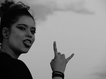 Portrait of young woman gesturing while standing against cloudy sky