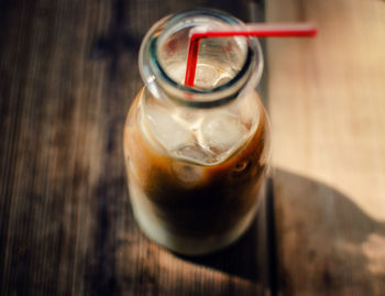 Close-up of iced coffee in glass bottle with straw on table