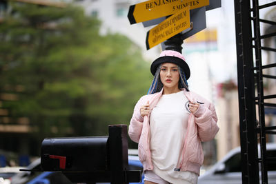 Portrait of young woman standing by street sign outdoors