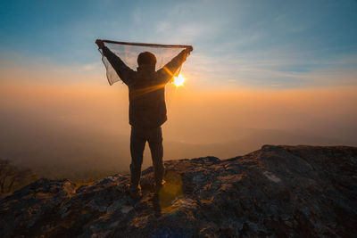 Woman standing on rock against sky during sunset