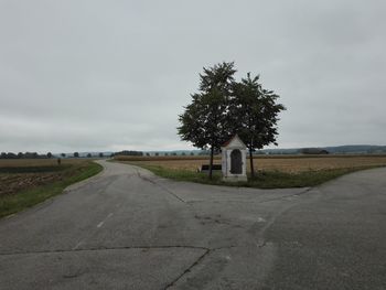 Road by trees on field against sky