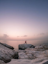 Man walking by sea on rock during sunset