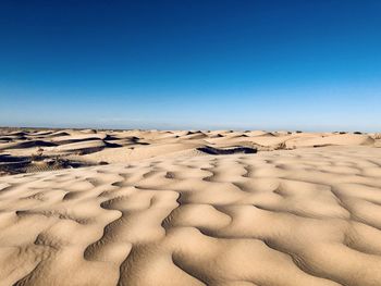 Sand dunes in desert against clear blue sky