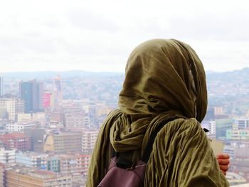 Rear view of woman wearing headscarf looking at view in city against sky