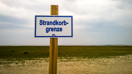 Warning sign on field against sky