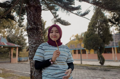 Portrait of smiling young woman standing against trees