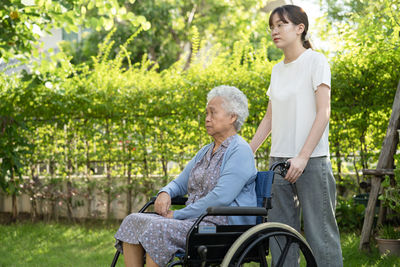 Caregiver help and care asian senior or elderly old lady woman patient sitting on wheelchair in park