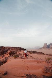 Rear view of man walking on sand at desert against sky