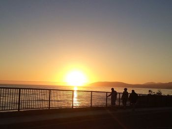 Silhouette people standing on beach against clear sky during sunset