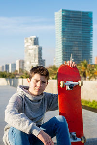 Teen sitting on skatepark ramp holding a skateboard, looking camera