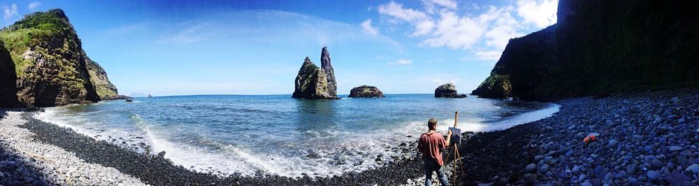 Panoramic view of man painting on shore against sky