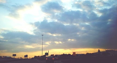 Cars on road against cloudy sky at sunset