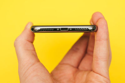 Close-up of human hand holding mobile phone against yellow background