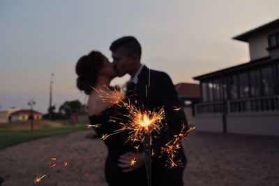 Couple kissing by lit sparkler in city