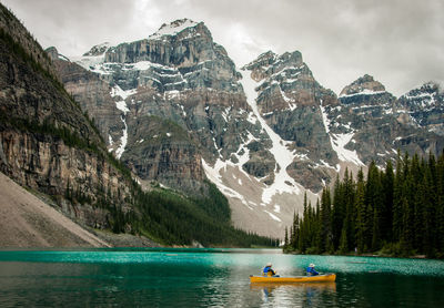 People sailing boat in lake against mountains