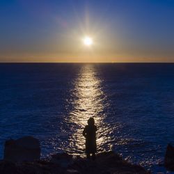 Silhouette of woman looking at sea during sunset