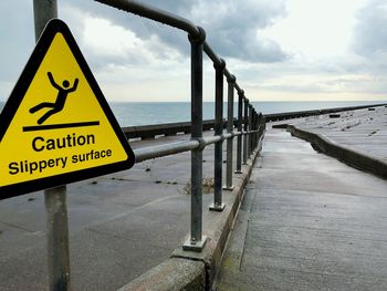 Information sign on railing by sea against sky