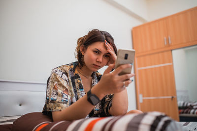 Portrait of young woman using mobile phone while sitting at home