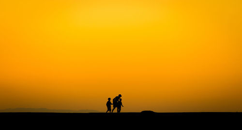 Silhouette people riding horse against orange sky