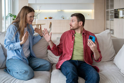 Sly husband cheater hiding smartphone display from unhappy nervous reproachful wife during quarrel