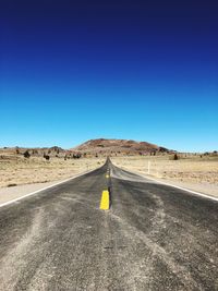 Road amidst desert against clear blue sky