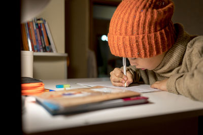 Boy wearing knit hat doing homework at table in apartment