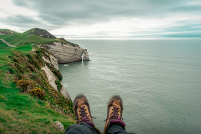 Low section of shoes by sea against sky