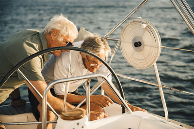 Smiling male friends navigating while sailing boat on sunny day