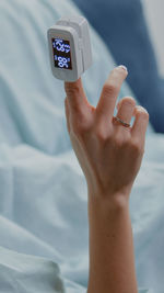 Cropped hand of woman holding alarm clock on bed