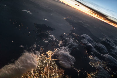 Aerial view of illuminated sea against sky during sunset