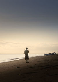 Rear view of woman walking at beach against sky during sunset