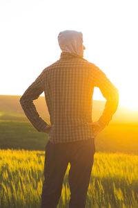 Rear view of man standing by grassy field against clear sky during sunset