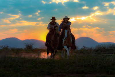 Horse riding horses on field against sky during sunset