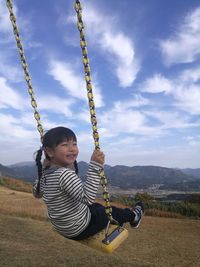 Girl sitting on swing at playground against sky