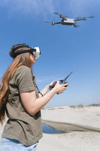 Rear view of woman using mobile phone at beach against sky