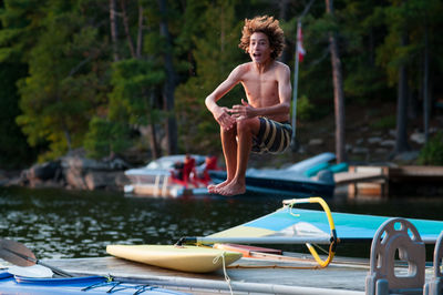 Shirtless boy jumping on boat in lake 
