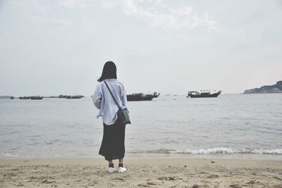 Rear view of man standing on beach against sky