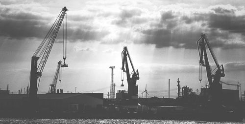 Cranes at construction site against cloudy sky