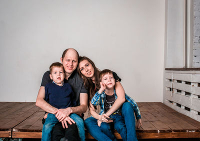 Smiling family holding house shape while sitting on hardwood floor at home