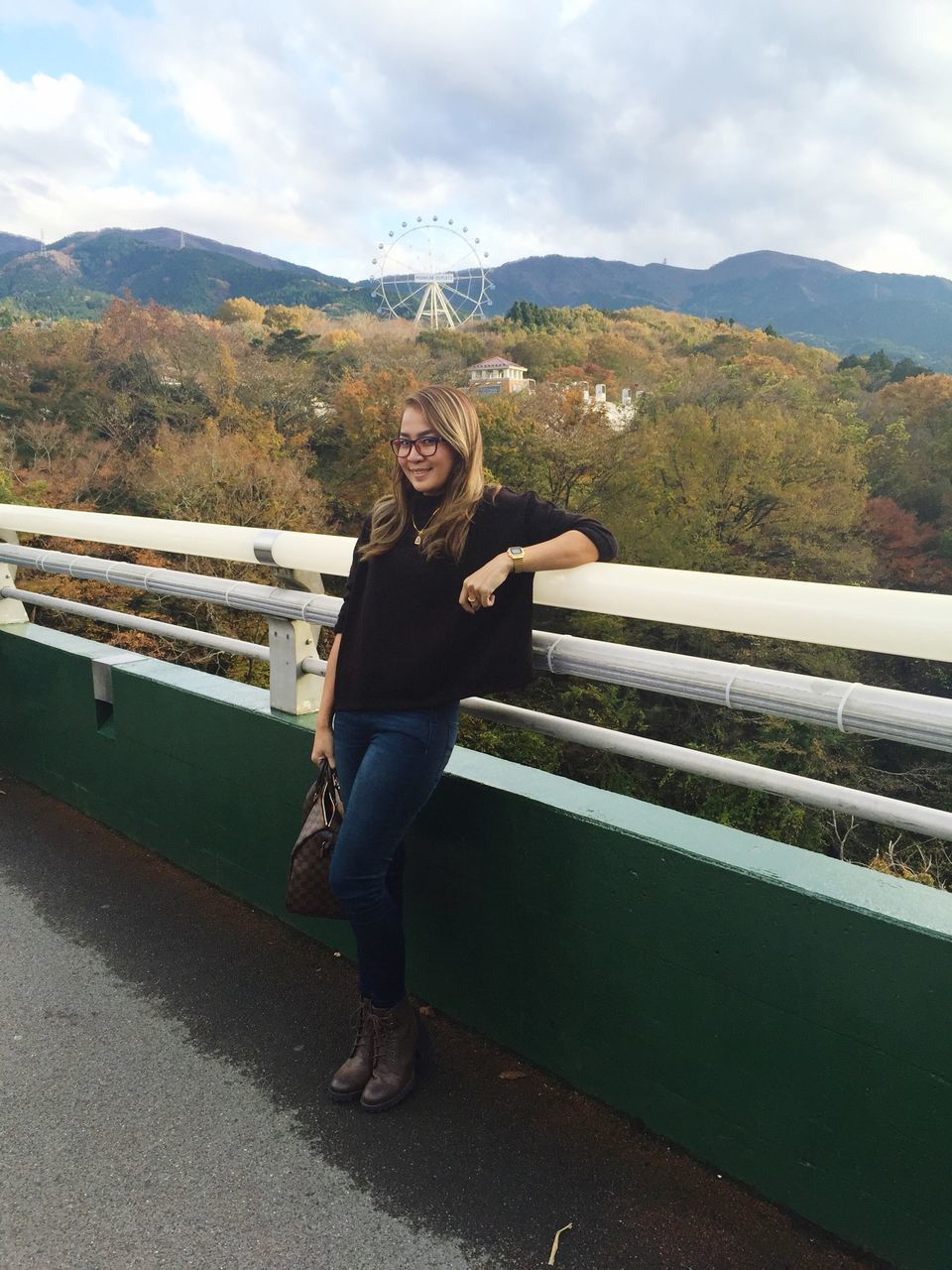 casual clothing, full length, lifestyles, young adult, mountain, person, leisure activity, standing, looking at camera, portrait, sky, young women, front view, smiling, mountain range, railing, day, three quarter length