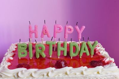 Close-up of birthday cake with burnt candles against pink background