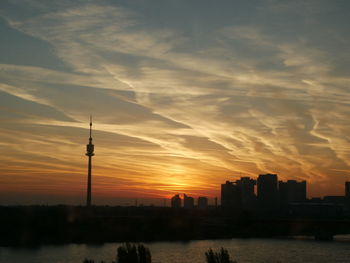 Silhouette of buildings against cloudy sky during sunset