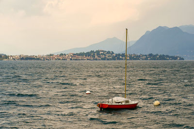 Red sailboat anchored on lake maggiore with coast and mountains in the background, piedmont, italy