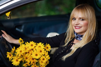 Portrait of smiling woman with red flower in car