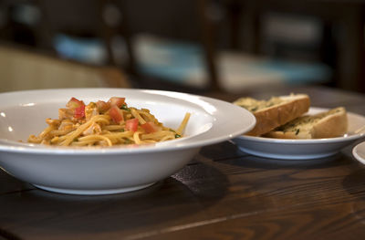 Close-up of spaghetti with garlic bread served in bowl on table